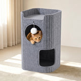 A gray felt cat tower with multiple levels and openings, shown in a sunlit room with an orange tabby cat peeking out from the circular upper compartment.