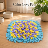 A square pet snuffle mat with concentric rings of light blue, purple, and yellow felt strips, displayed on a light wood floor in a bright room with a plant and bowls.