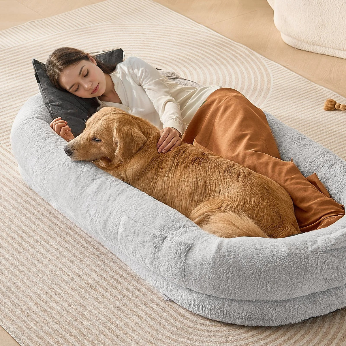 Woman lying on a large dog bed with a golden retriever, both resting on a beige carpet.
