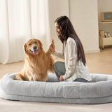 Woman giving a high-five to a golden retriever on a large dog bed in a room with light-colored walls and wooden flooring.