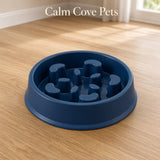 A dark blue pet slow feeder bowl with a textured, ribbed interior, shown on a light wood floor in a home setting. The text 'Calm Cove Pets' is displayed at the top.
