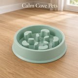 A light mint green pet slow feeder bowl with a textured, raised anti-slip design, shown on a light wood floor with the text 'Calm Cove Pets' at the top.