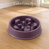 A purple slow-feeder pet bowl with textured, raised nubs inside, shown on a light wood floor in a room setting. The text 'Calm Cove Pets' is displayed at the top.