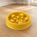 A yellow high-side slow feeder pet bowl placed on a light wood floor in a bright room, with the text 'Calm Cove Pets' at the top.